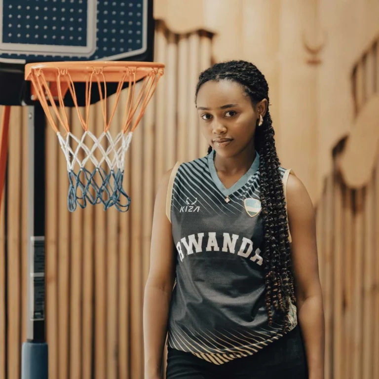 Rwandan woman in KIZA black basketball jersey with Imigongo details and Rwandan flag badge